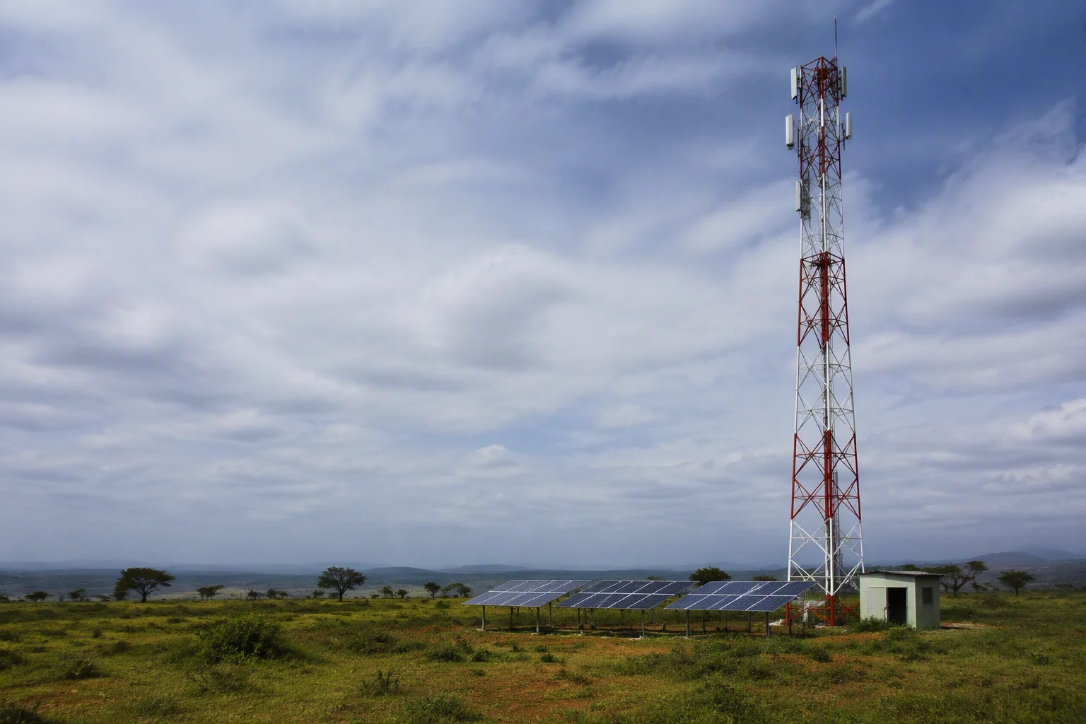 Telecom tower in an African savanna with solar panel racks beside it and a dramatic sky