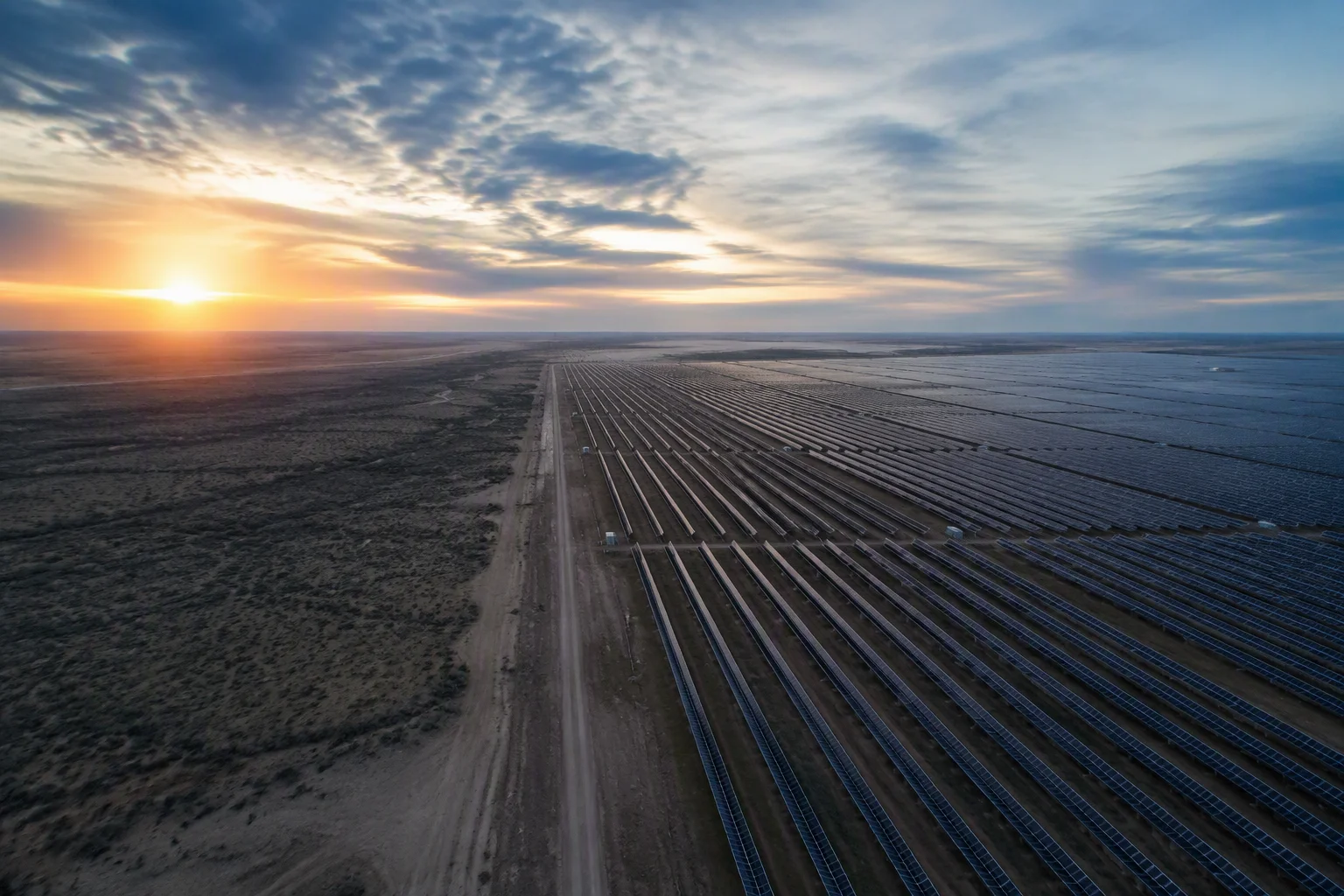 Massive utility-scale solar farm with single-axis trackers at dawn, rows vanishing to the horizon